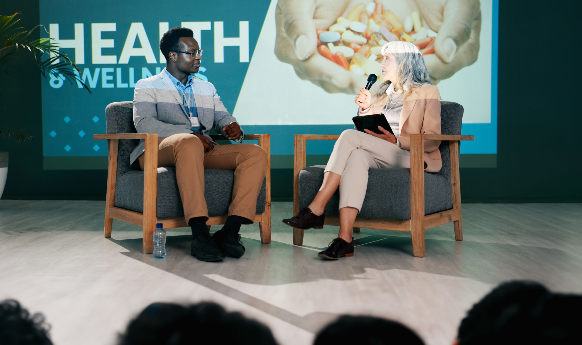 Health convention, speaker and speech of woman on stage with host on mic and tablet at event. Workshop, talk and conference presentation on wellness, pharma or medical innovation of drugs with guest